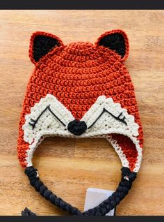 a crocheted fox hat is shown on a wooden surface with a tag attached to it