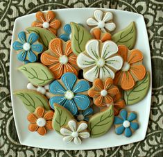 decorated cookies in the shape of flowers on a white plate with green and orange leaves