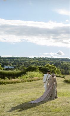 a bride and groom are standing in the middle of a grassy field under a blue sky