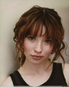 a close up of a person wearing a black top and hair in a messy bun