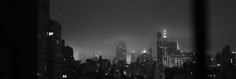 the city skyline is lit up at night in black and white, as seen through a window