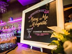 there is a sign on the bar that says marry me margarita with wine glasses and flowers