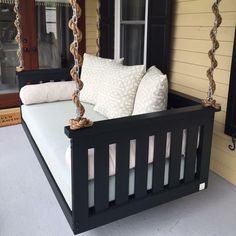 a black porch swing bed with white pillows on the front and back cushions, in front of a yellow house