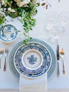 the table is set with blue and white plates, silverware, and floral centerpieces