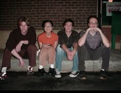 four young men sitting on a bench in front of a brick building at night time