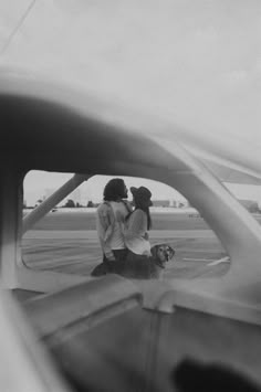 two people and a dog are standing in front of an airplane window looking out at the tarmac