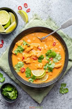 a bowl filled with soup and garnished with cilantro, limes, red peppers, and sliced jalapenos