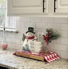 a kitchen counter topped with white dishes covered in snowman figurines next to a window