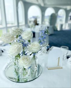 white roses and blue flowers in glass vases on a table at a wedding reception