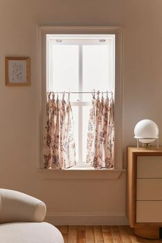 a white chair sitting in front of a window with curtains hanging from it's sides