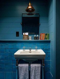 a bathroom with blue tiles and a white sink in the corner next to a book shelf