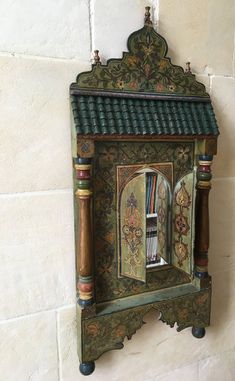 an ornate wooden clock mounted to the side of a white brick wall with green and gold accents