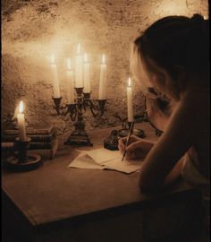 a woman writing on a piece of paper in front of candles