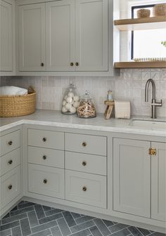 a kitchen with gray cabinets and white counter tops, along with a basket on the sink