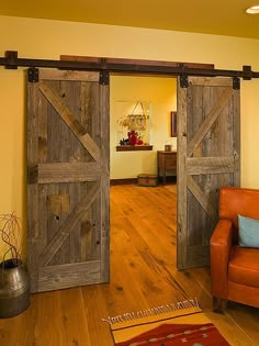 an open barn door in a living room with wooden floors and orange chair, yellow walls