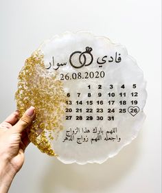 a person holding up a white and gold plate with a date in arabic on it