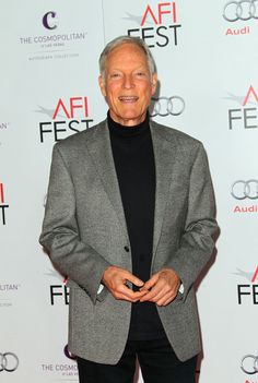 an older man in a gray jacket and black turtle neck sweater standing on a red carpet