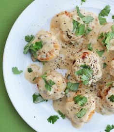 a white plate topped with scallops covered in gravy and garnished with parsley