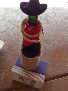 a wine bottle with a cowboy hat tied to it sitting on top of a box