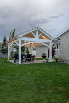 a covered patio with an outdoor dining table and grill in the back yard at dusk