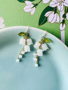 Experience the timeless elegance of White Jade Lily of the Valley Flower Earrings, a stunning handmade accessory that celebrates the natural beauty of this delicate bloom. These earrings are meticulously crafted with care and precision, showcasing the ethereal allure of lily of the valley flowers, accented by lush green leaves, all fashioned from white jade. Each earring features trio meticulously carved white jade lily of the valley flower, capturing the essence of this beloved bloom in its ful May Birth Month Flower, Lily Of The Valley Flowers, Valley Flowers, Birth Month Flower, Month Flowers, White Jade, Birth Month Flowers, Birth Month, Lily Of The Valley