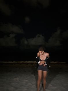 a woman standing in the sand at night with her back turned to the camera,