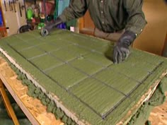 a man in black gloves is working on a green table cloth that has been cut into squares