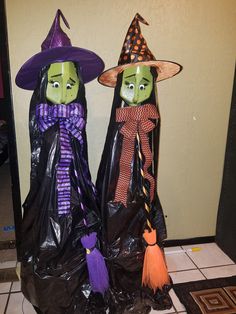 two plastic witches standing next to each other on a tile floor in front of a wall