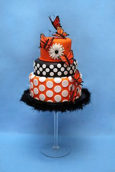 a three tiered cake decorated with orange and black polka dots, butterflies and feathers