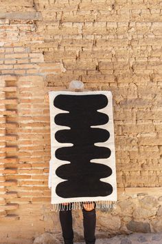 a person standing in front of a brick wall with a black and white rug on it