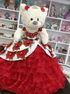 a white teddy bear wearing a red and white dress with roses on it's skirt