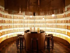 a bar with three stools in front of a wall full of bottles on it