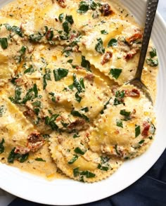 a white plate topped with ravioli covered in cheese and spinach sauce next to a fork