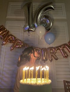 a woman blowing out candles on a birthday cake with balloons and streamers around her