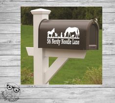 a mailbox with an image of horses and sheep on it, in front of a wooden fence