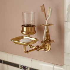 two toothbrushes and a cup on a gold plate in a bathroom wall holder