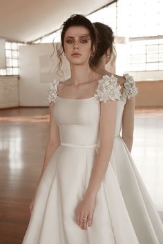 a woman in a white dress standing on a wooden floor with her hands behind her back