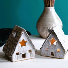 two ceramic houses are sitting on a table next to a vase with flowers in it