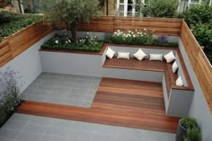 a wooden bench sitting on top of a cement floor next to a garden filled with plants