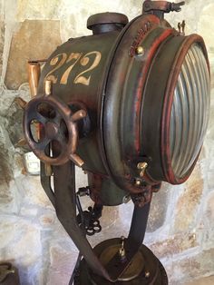 an old fashioned steam engine sitting on top of a metal stand in front of a stone wall