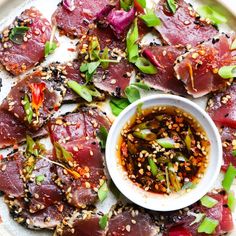 a platter filled with sliced up meat and garnished with sesame seeds on top