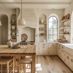 a large kitchen with wooden floors and white cabinets, an island in the middle is surrounded by open shelving