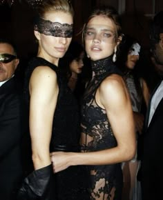 two beautiful women standing next to each other in front of a man wearing a mask