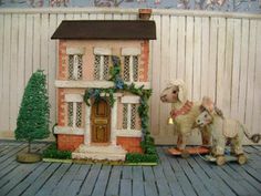 two figurines sitting on top of a wooden floor next to a small house