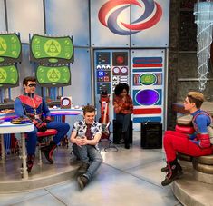 three men sitting on chairs in front of a tv set