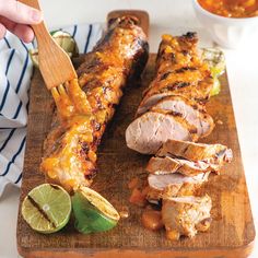 a person cutting up some meat on a wooden cutting board with limes and sauce