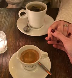 two people holding hands over a cup of coffee on a table with spoons and candles