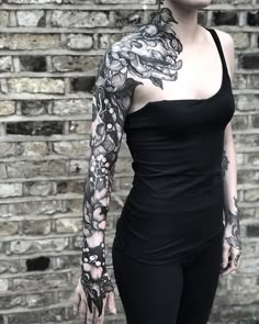 a woman with tattoos standing in front of a brick wall