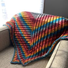 a multicolored crocheted blanket sitting on top of a couch next to a window