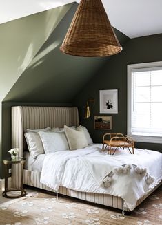 a bedroom with green walls, white bedding and a wicker basket hanging from the ceiling